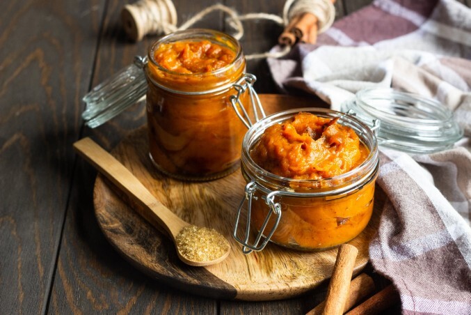 Hausgemachtes Kürbischutney Zwei Bügelgläser mit hausgemachtem Kürbischutney werden auf einem rustikalen Holzbrett präsentiert.