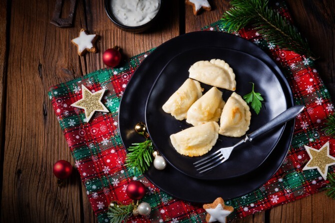 Ein schwarz Teller mit vegetarischen Steinpilzmaultaschen steht auf einen weihnachtlich dekorierten Tisch.